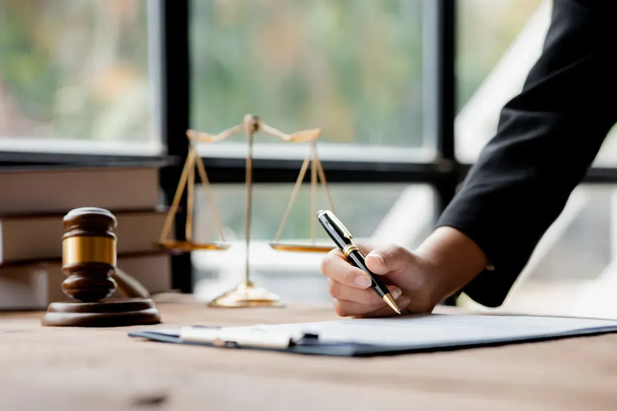 Martillo, balanza de la justicia y persona escribiendo en papel en un escritorio, posiblemente un despacho de abogados .