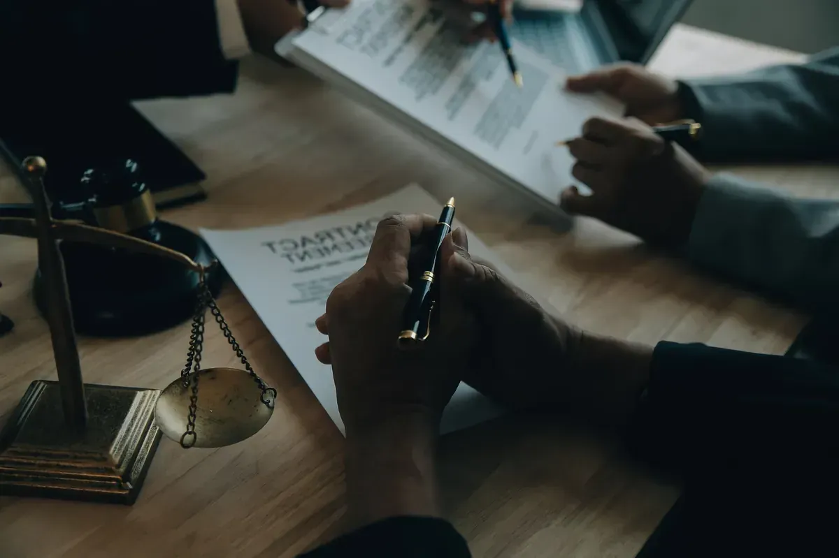 Personas firmando documentos en una mesa; balanza de la justicia en primer plano.