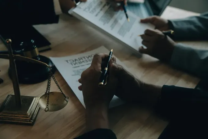Personas firmando documentos en una mesa; balanza de la justicia en primer plano.