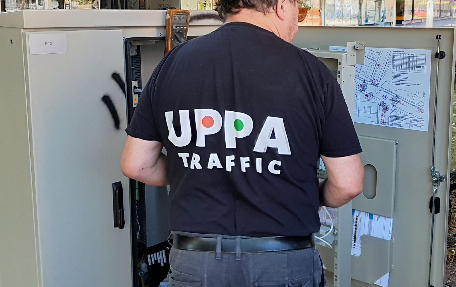 Liikennevalot ja suojatiepainike pylväissä. Liiviin pukeutunut henkilö työskentelee yhdellä painikkeella.