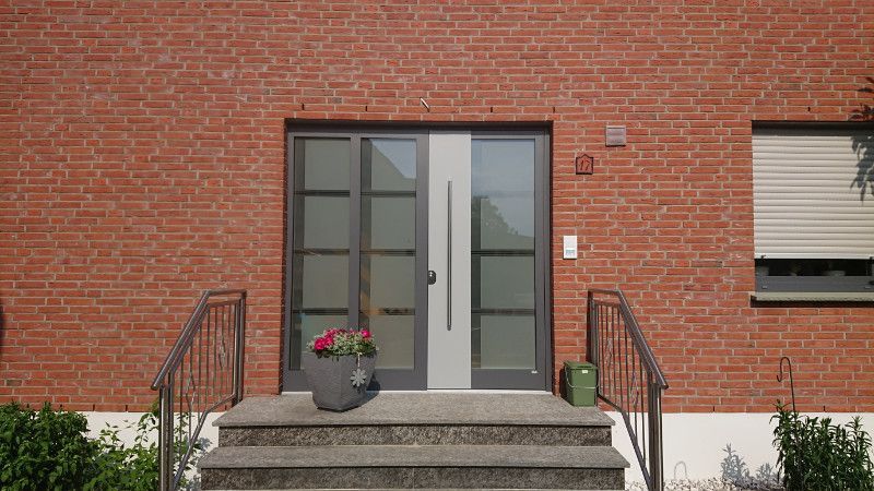 eine rote Backsteinmauer mit einer modernen Eingangstür und Schritten .