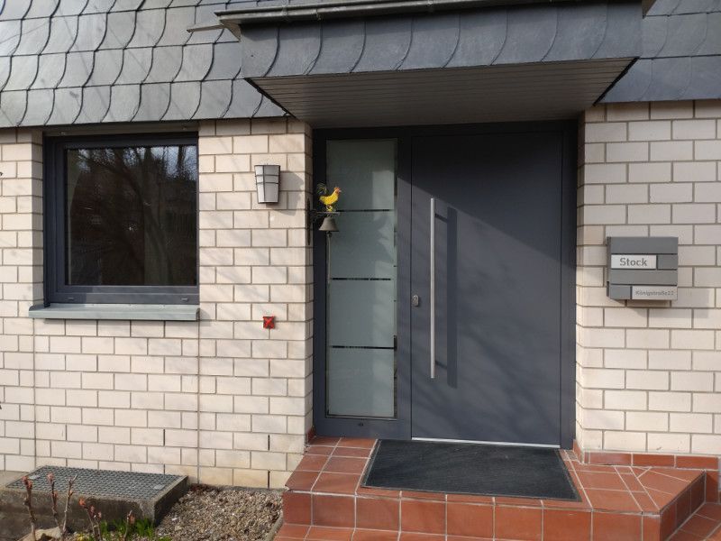 eine graue Haustür mit einem Fenster und einem Briefkasten