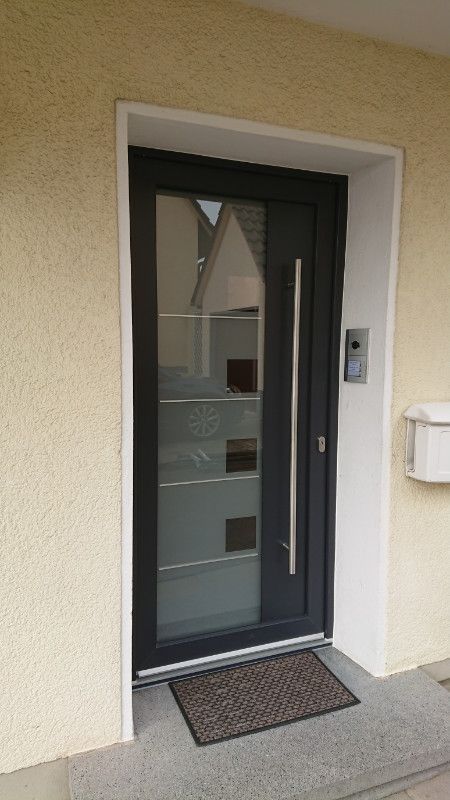 eine schwarze Haustür mit einem silbernen Griff und einer Türmatte .