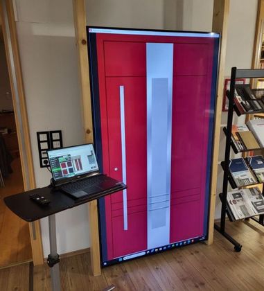 ein Laptop sitzt auf einem Tisch neben einer roten Tür auf einem 85 Zoll Bildschirm