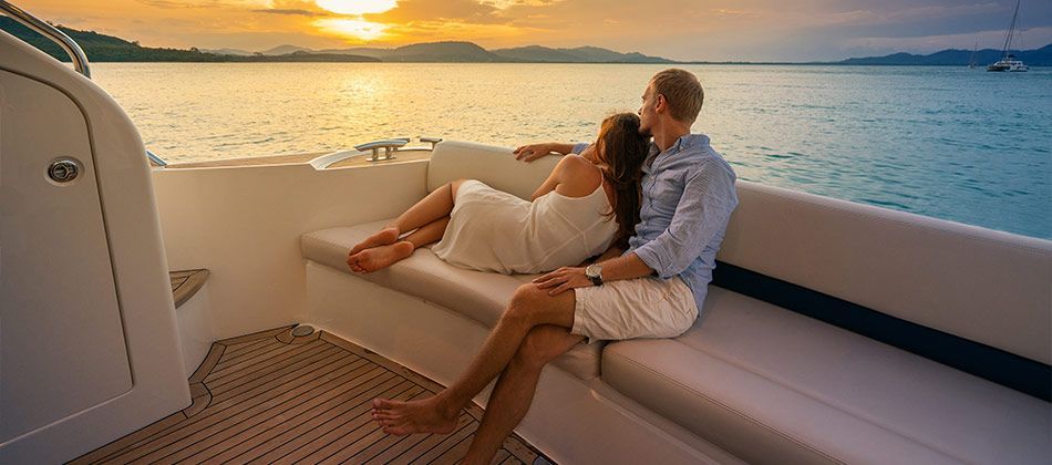 Couple assis sur la banquette d'un yacht face à un coucher de soleil