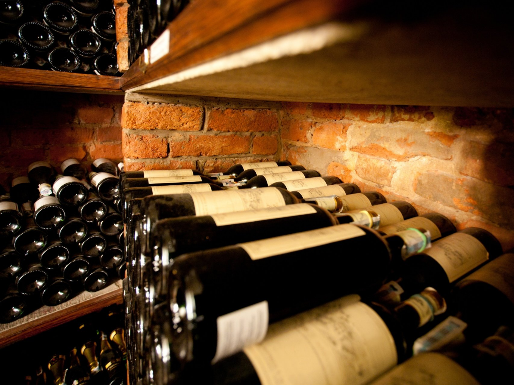 Des bouteilles de vin rangées à l'horizontale sur des étagères dans une cave aux murs de briques.