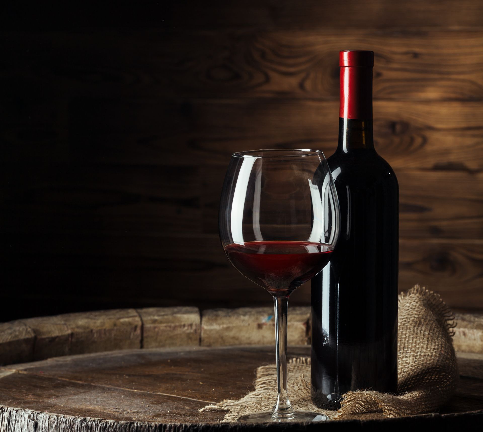 Bouteille et verre de vin rouge, posés sur un tonneau en bois.