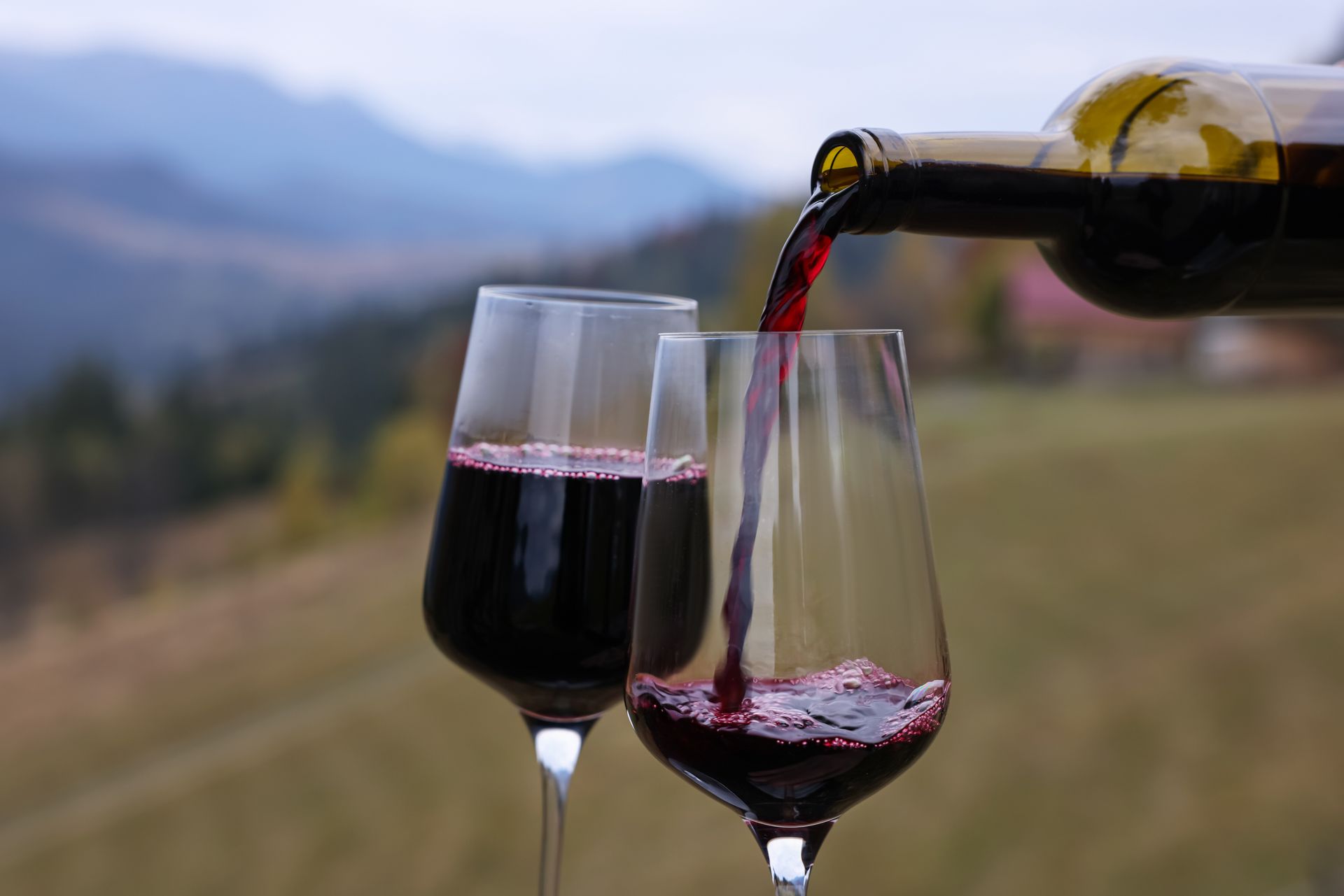 Du vin rouge est versé dans deux verres, avec les montagnes en arrière-plan.