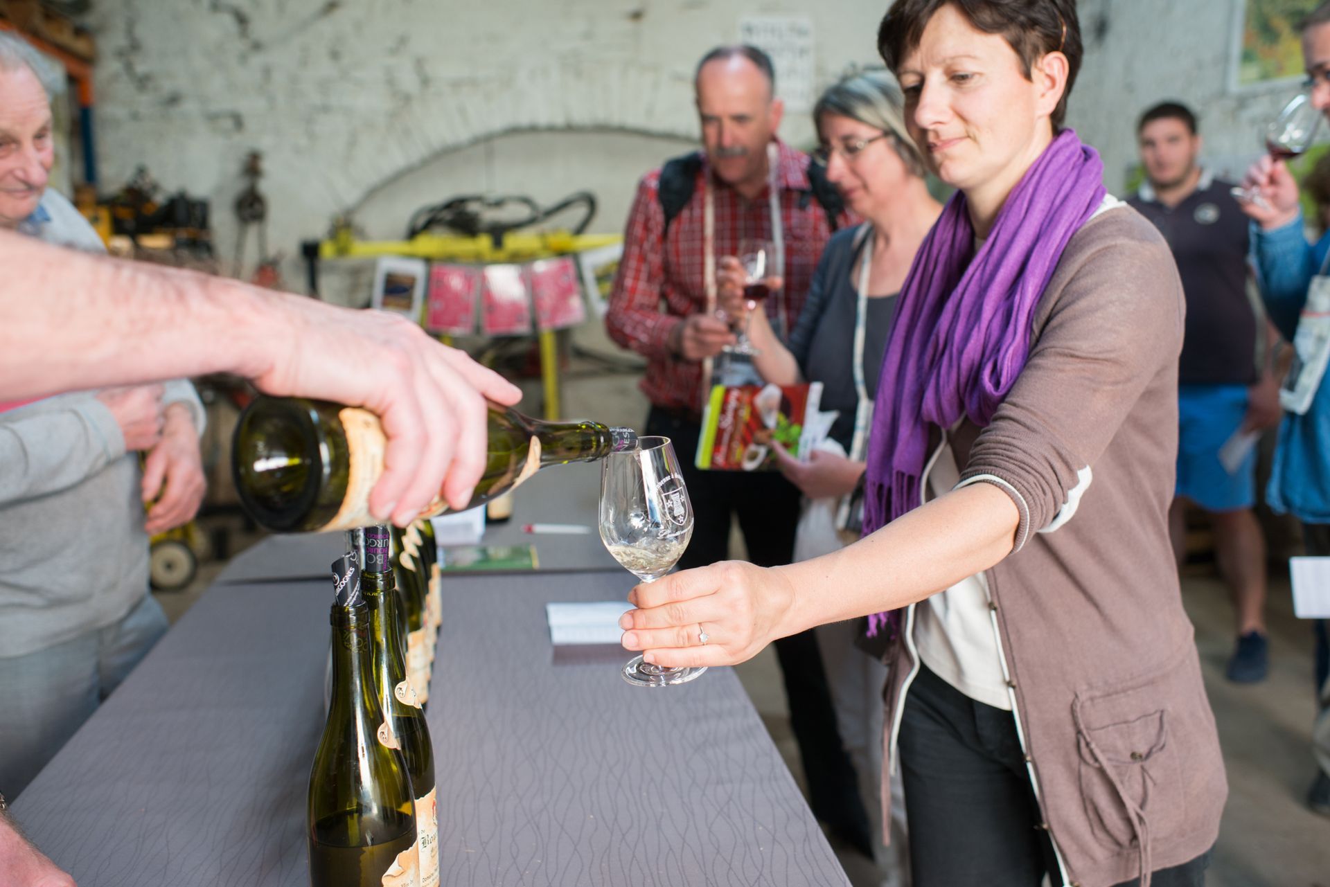 Une personne verse du vin dans un verre lors d'une dégustation, sous le regard des autres participants.