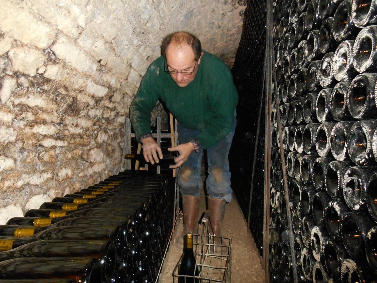 Un homme en chemise verte et jean manipule des bouteilles dans une cave à vin.