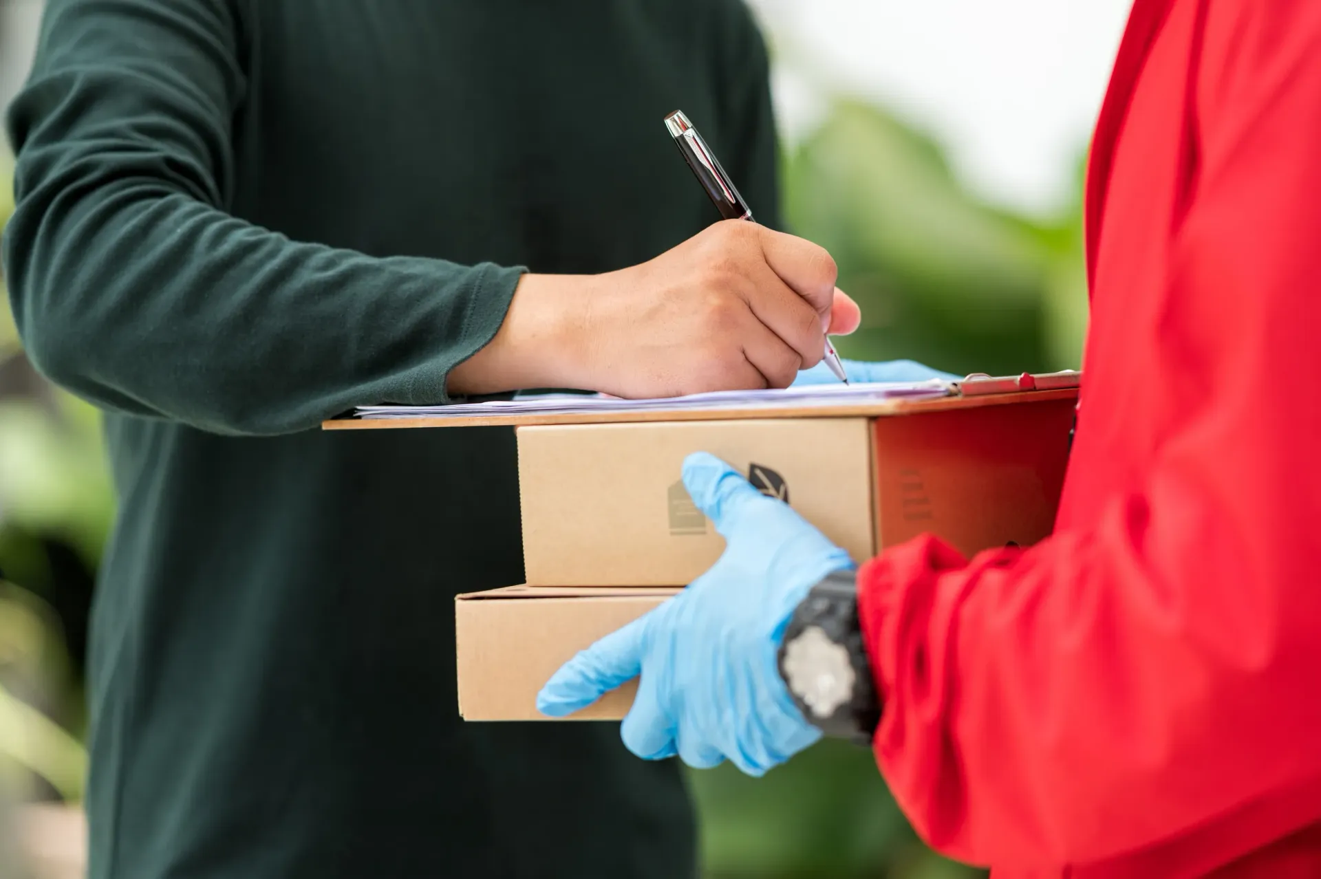 Persona firmando la entrega de dos cajas de cartón; repartidor vestido de rojo y con guantes azules.