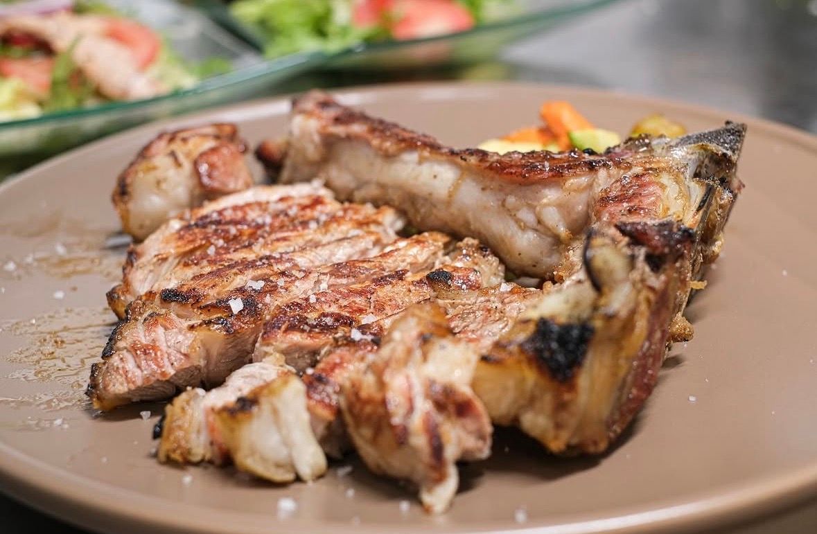 Trozos de filete a la parrilla en un plato, con una ensalada borrosa al fondo.