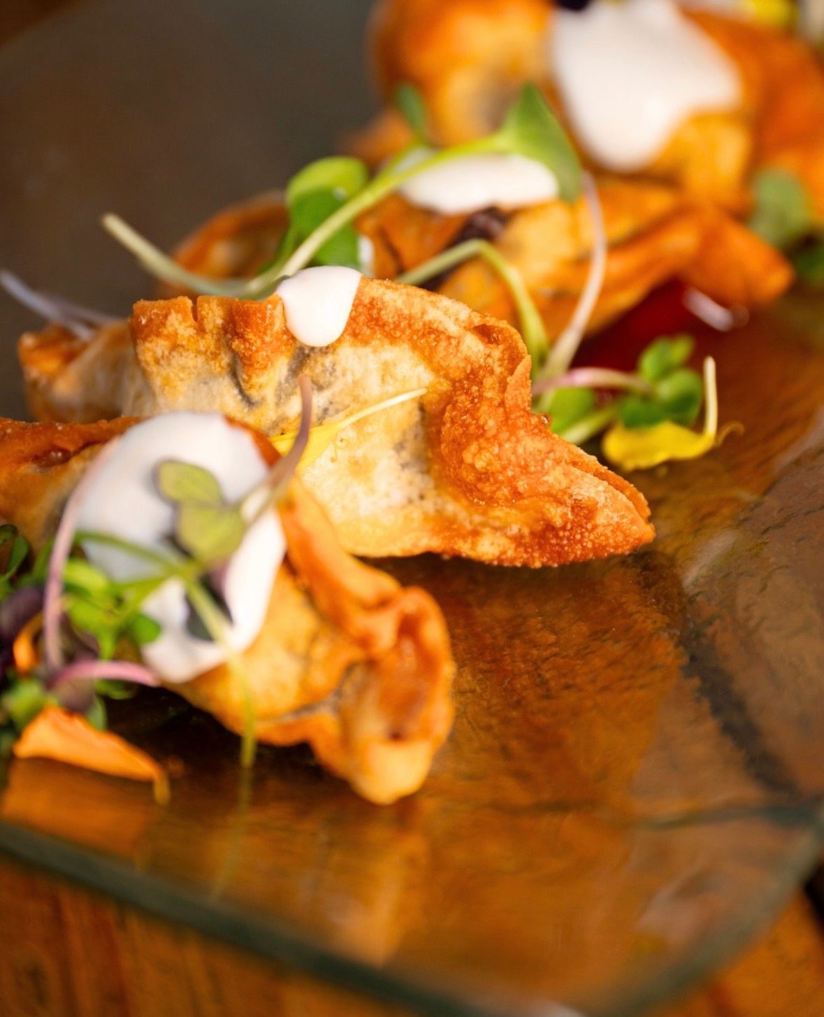 Aperitivos fritos crujientes en un plato de cristal, cubiertos con verduras y un chorrito de glaseado blanco
