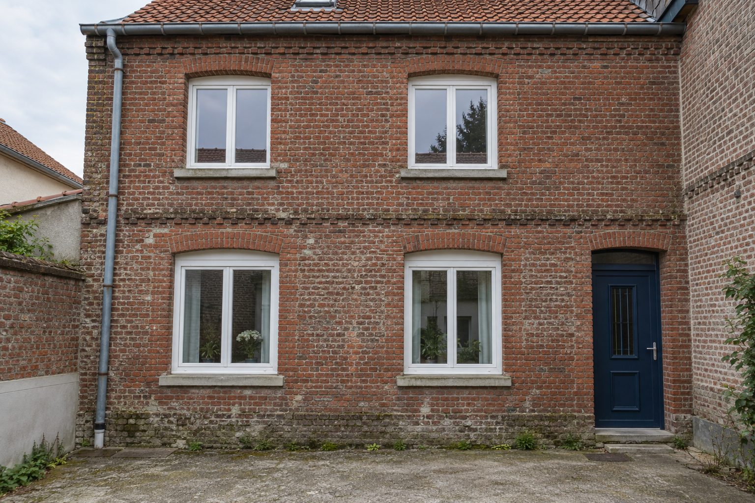 Façade de maison en briques avec quatre fenêtres et une porte d’entrée bleu foncé