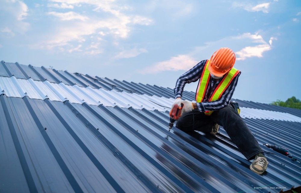 Arbeiter mit Schutzhelm und Sicherheitsweste montiert Metalldachplatten auf einem Dach