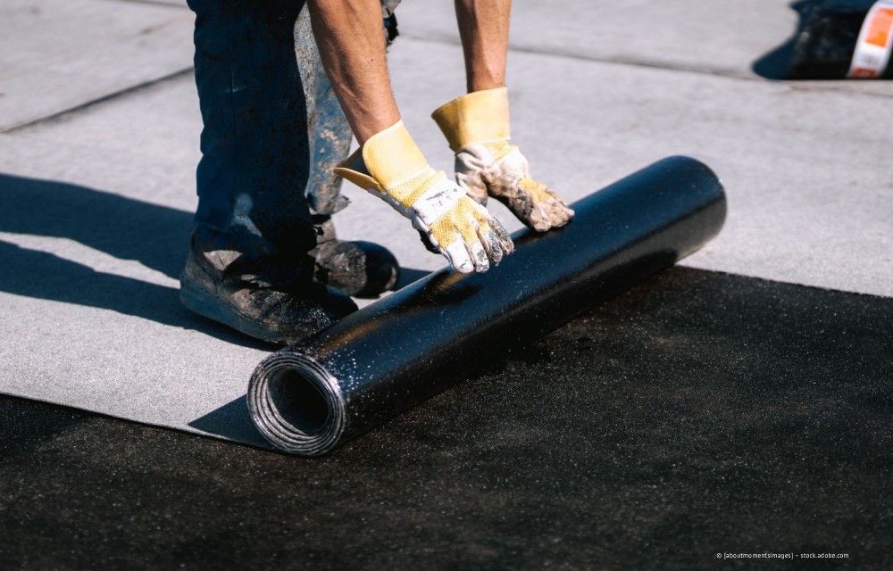 Arbeiter rollt schwarze Dachmembran auf ein Flachdach