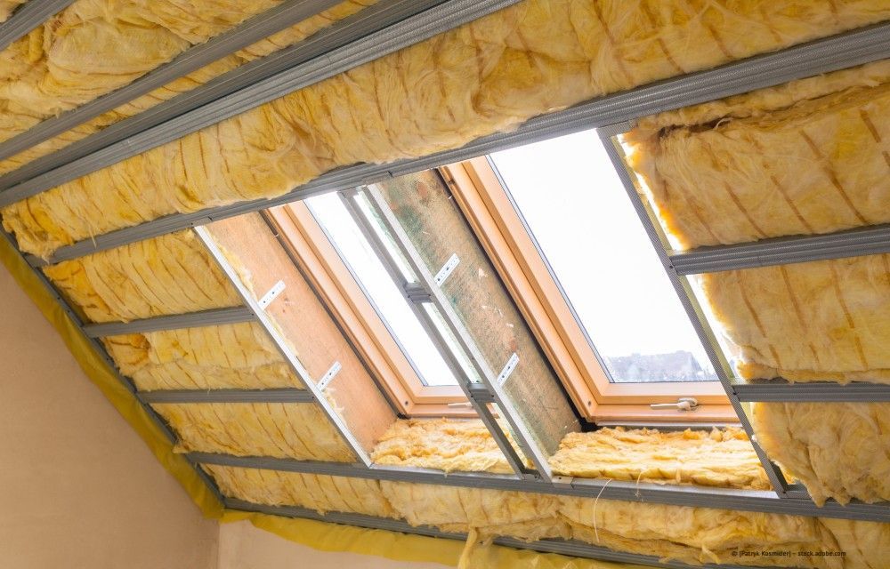 Dachboden mit gelber Dämmung und einem von Metallträgern eingefassten Dachfenster