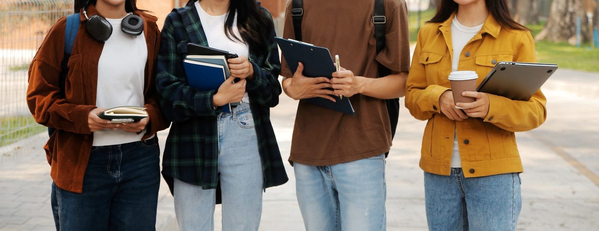 Cuatro personas de pie al aire libre, sosteniendo cuadernos y leyendo juntas en una calle.