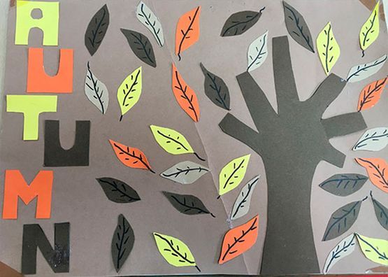 Mural otoñal en el aula con un árbol, hojas coloridas y la palabra 