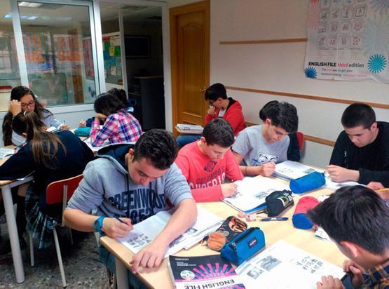 Estudiantes sentados en sus pupitres, escribiendo en sus cuadernos durante una sesión de estudio en el aula.