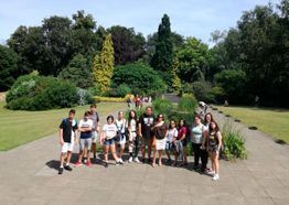 Grupo de personas posando en un sendero pavimentado en un parque soleado con árboles y vegetación al fondo.