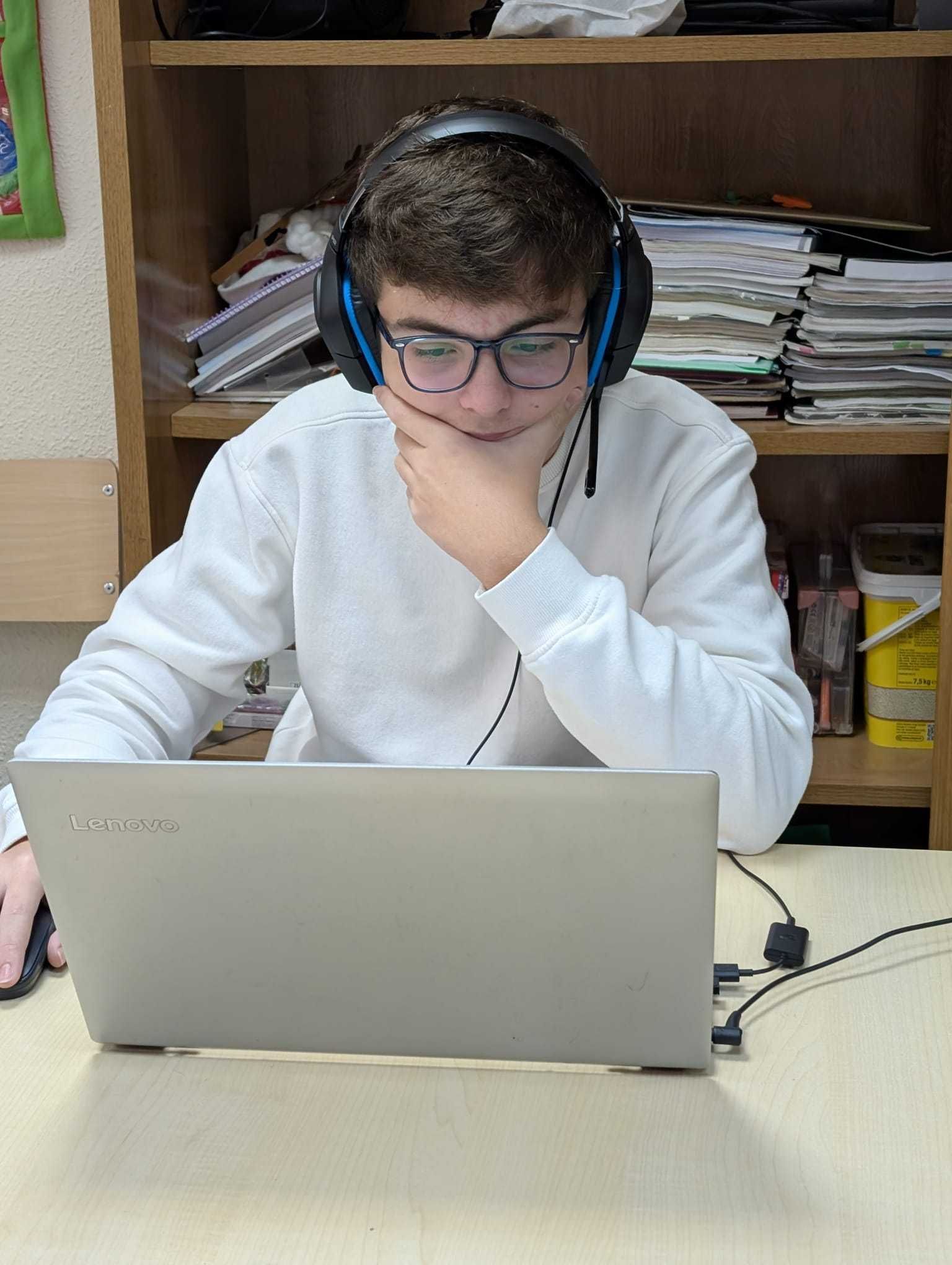 Persona con auriculares y gafas, sentada frente a un ordenador portátil en un aula o zona de estudio.
