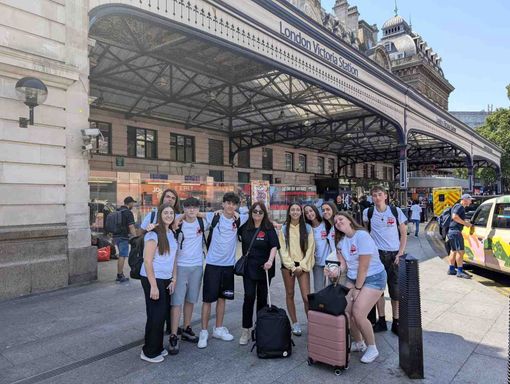 Grupo de viajeros con maletas posando frente a una gran estación de tren bajo una gran marquesina.