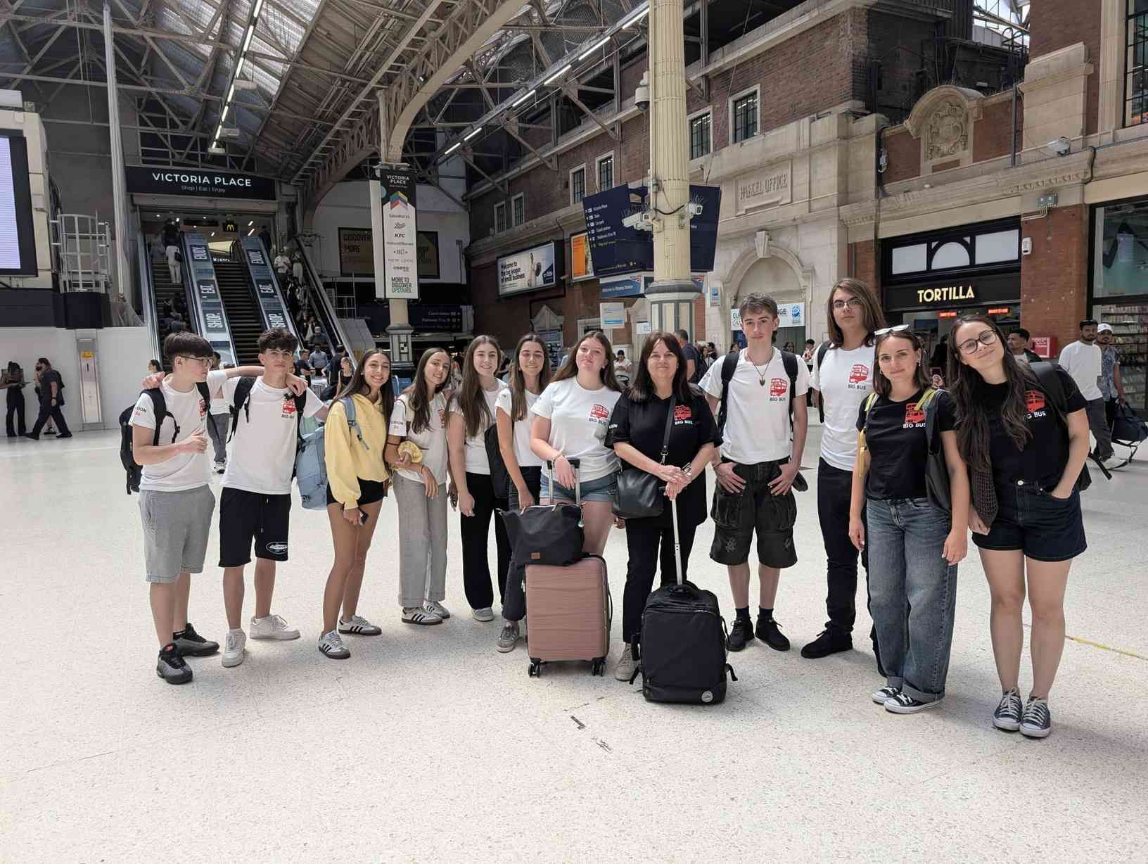Grupo de viajeros de pie con su equipaje en el vestíbulo de una gran estación de tren.