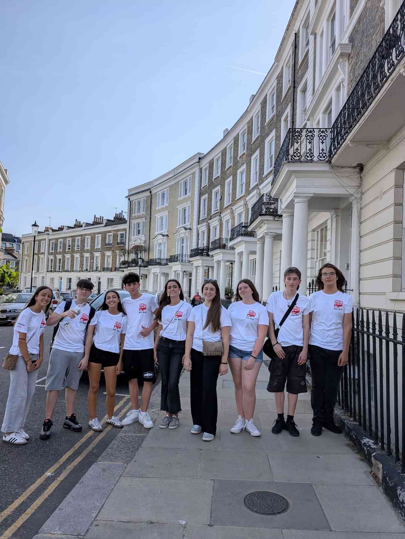 Grupo de personas con camisetas blancas posando en una calle soleada con edificios blancos curvos detrás.
