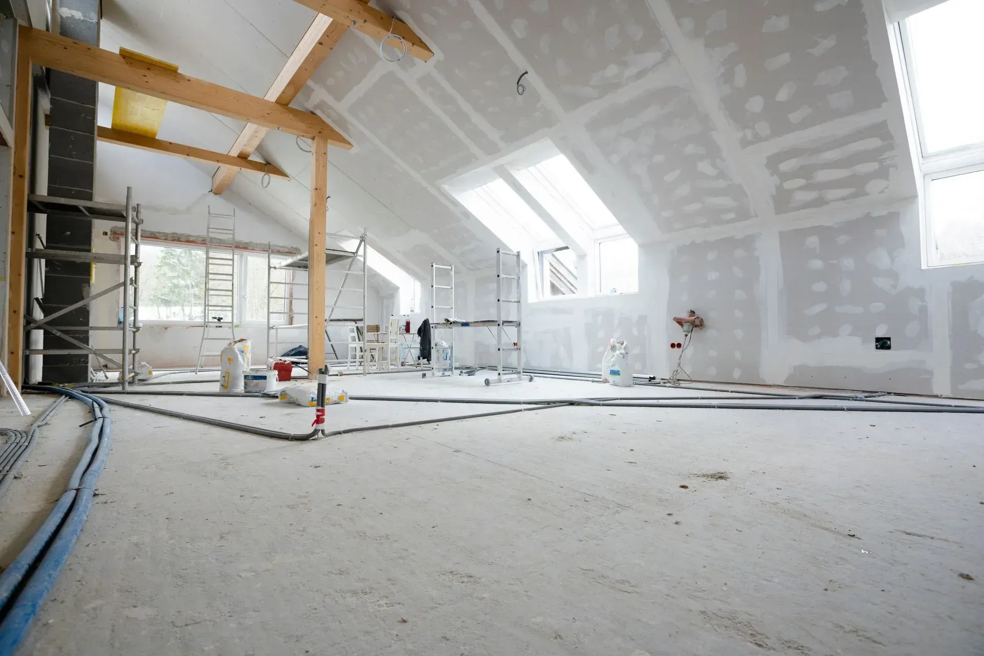 Combles rénovés avec murs en plaques de plâtre blanches, fenêtres de toit, poutres apparentes et sol brut en cours de travaux