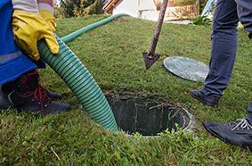 Un hombre está bombeando agua a un tanque séptico con una manguera verde.