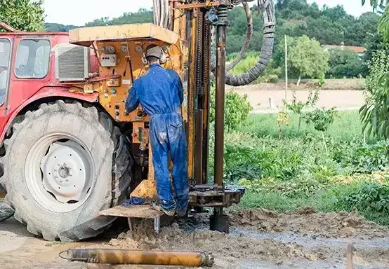 Un hombre está trabajando en un pozo de agua con un tractor al fondo.