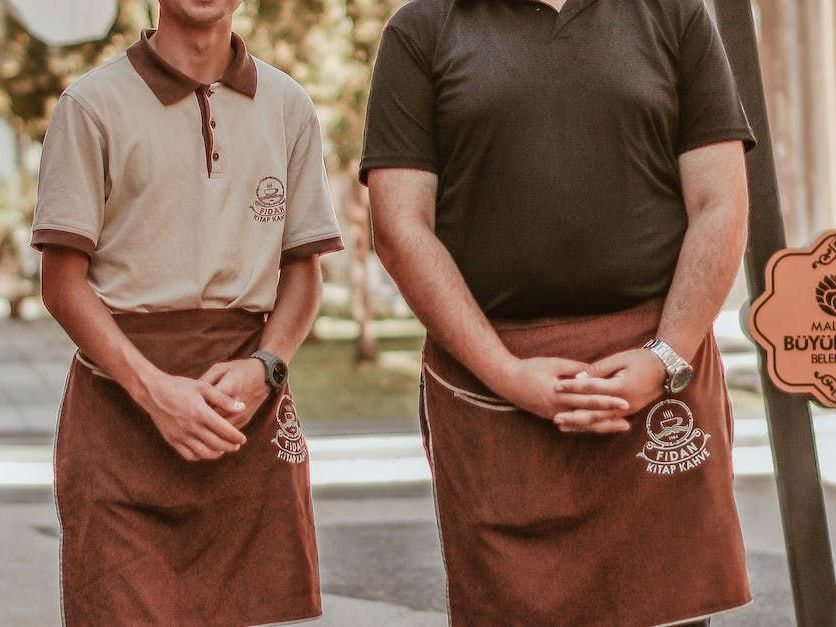 zwei Männer stehen nebeneinander und tragen braune Schürze mit der Aufschrift fidan kahve darauf