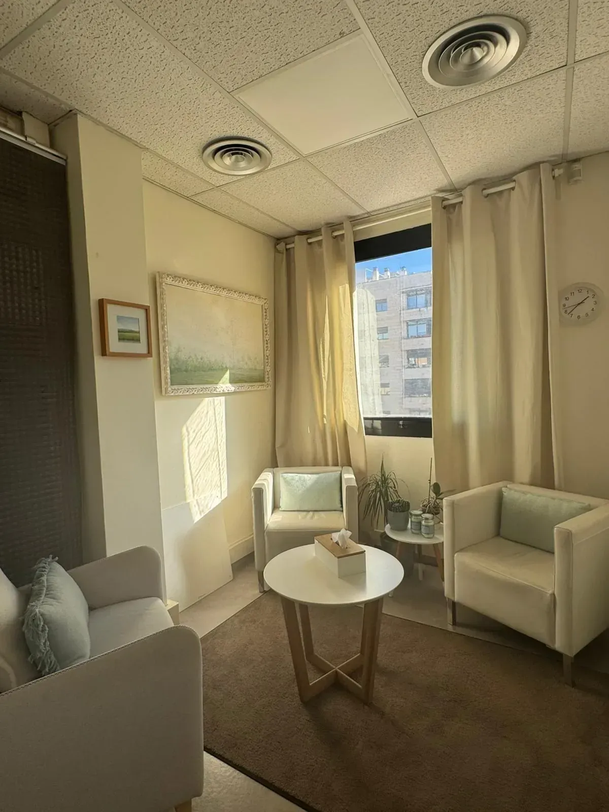 Acogedora sala de asesoramiento con sillas blancas, mesa pequeña, obras de arte y luz natural.