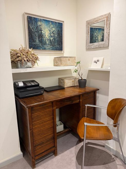 Escritorio de madera en un nicho, con una laptop, un teléfono y objetos decorativos. Silla junto al escritorio y arte en la pared.