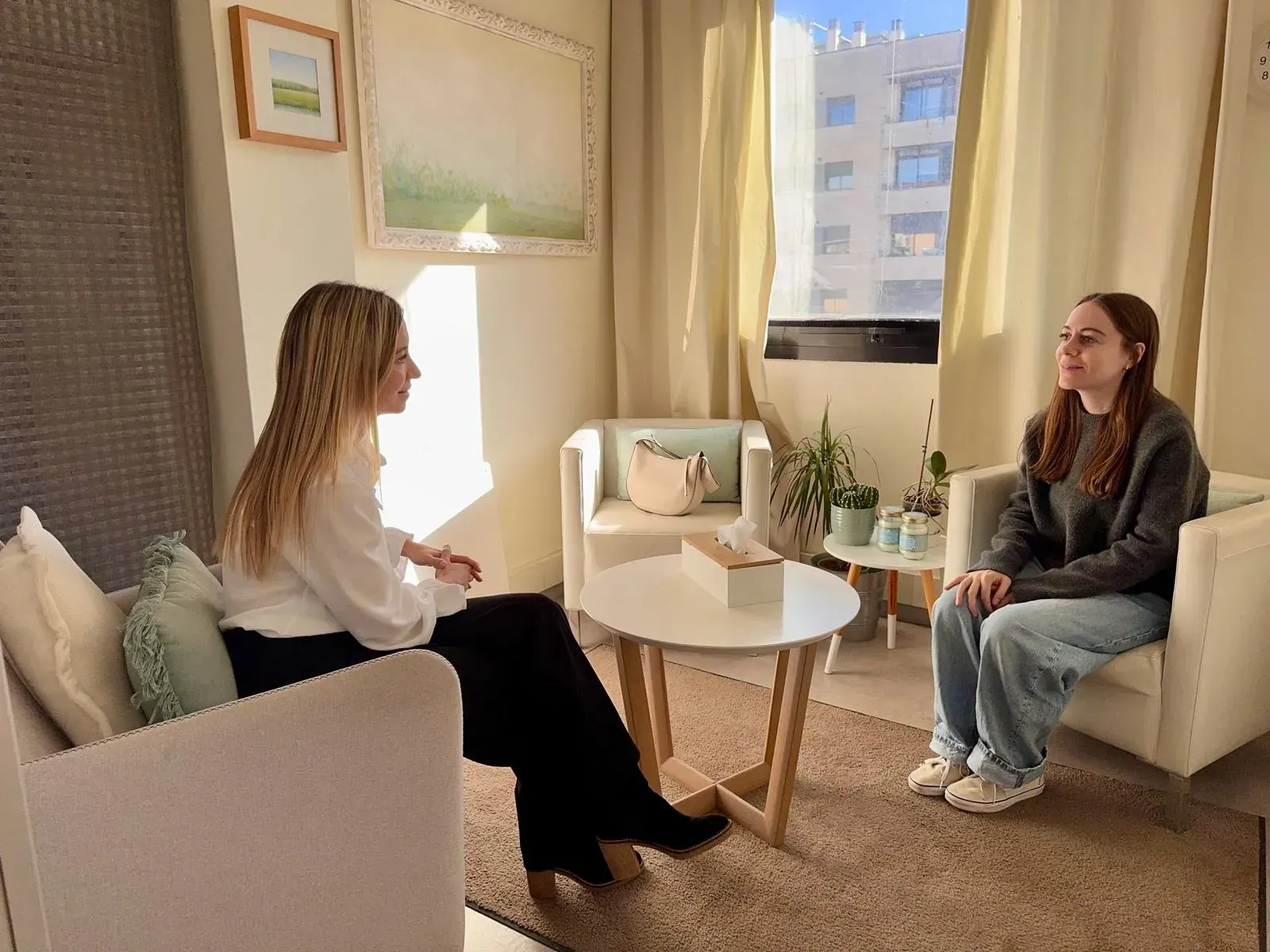 Terapeuta y paciente sentados en una oficina, discutiendo problemas. Ambiente luminoso, tonos neutros.