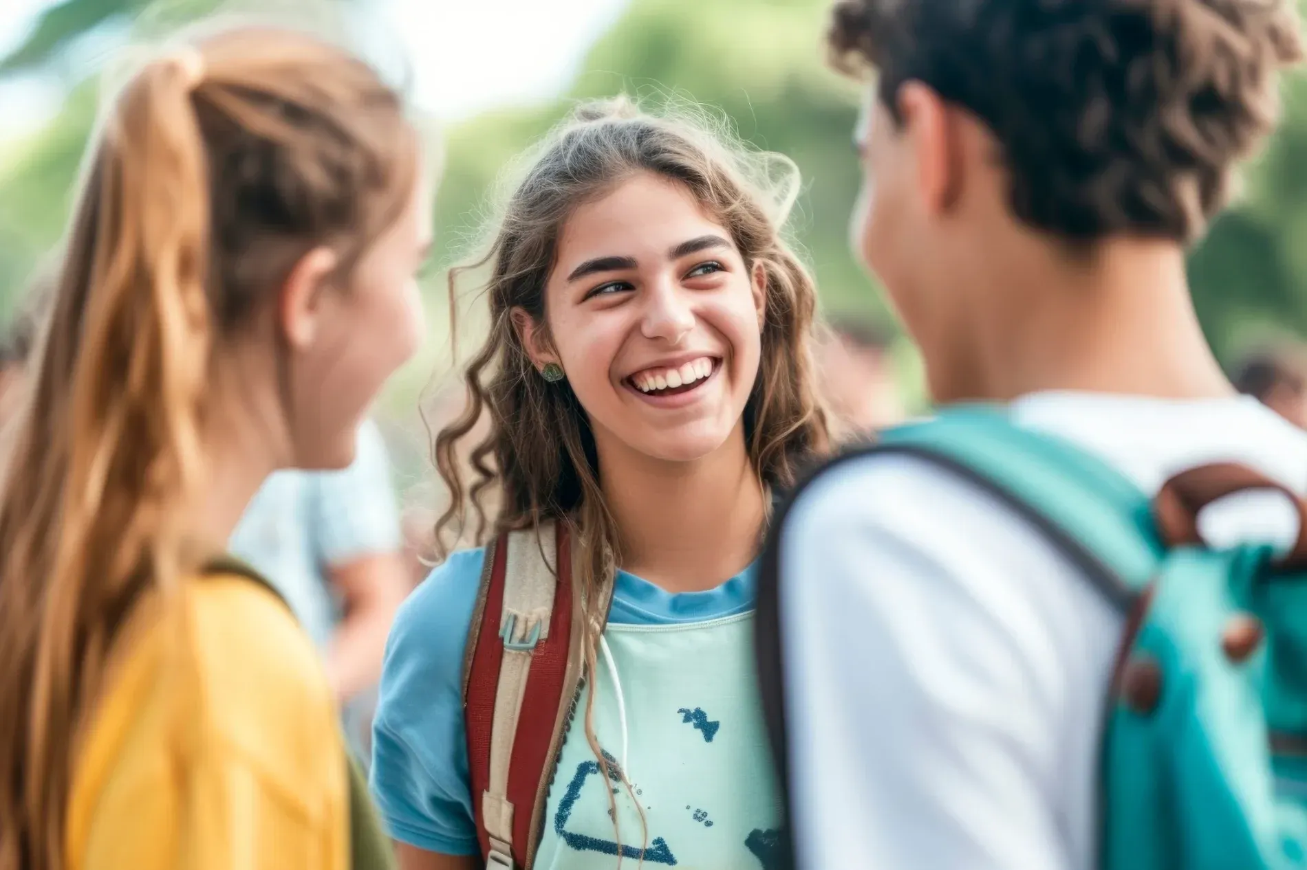 Tres jóvenes sonriendo y conversando al aire libre; uno lleva una mochila.