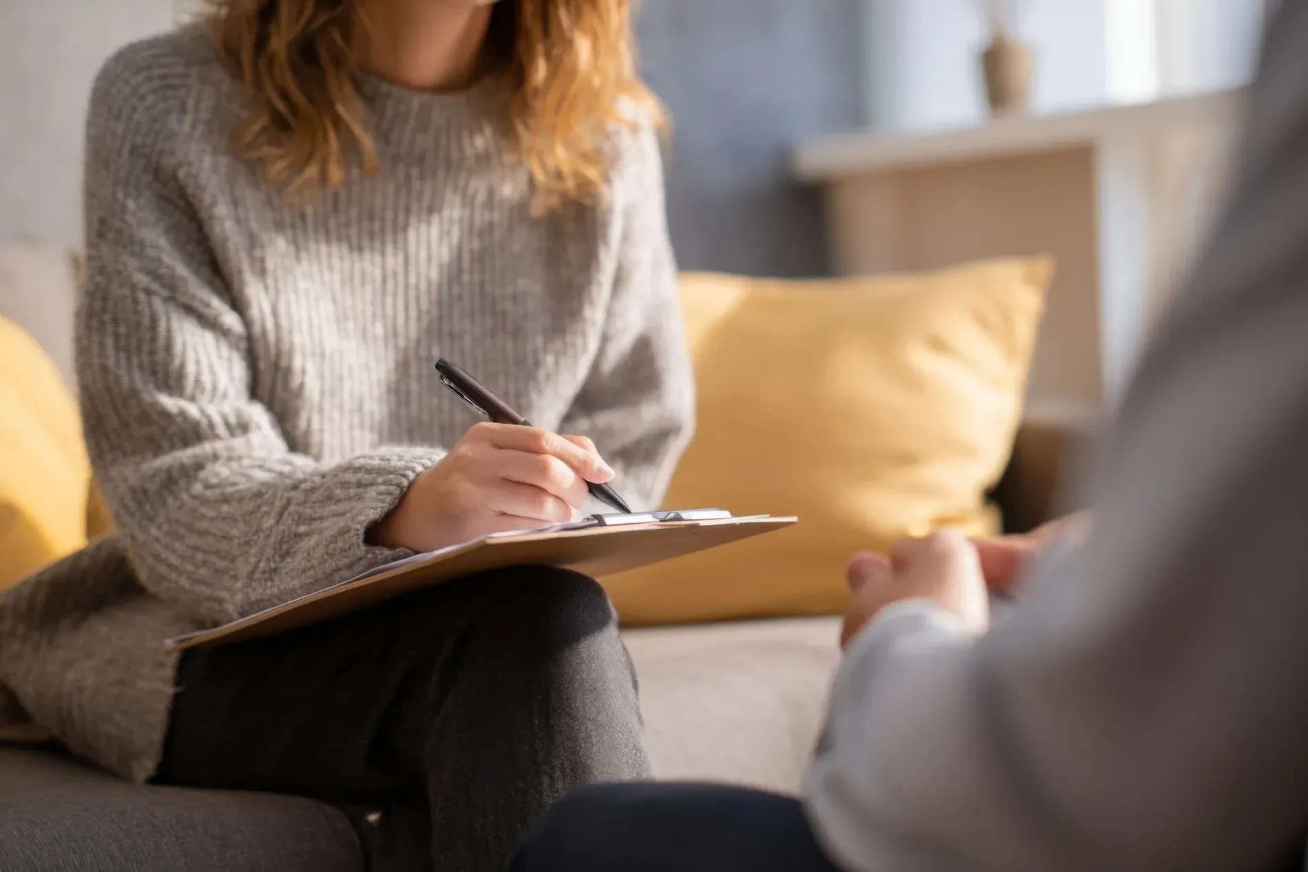 Terapeuta tomando notas mientras consulta con una persona en un diván.