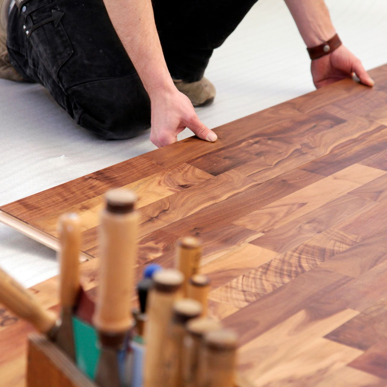 Gros plan sur les mains d'un professionnel en train de poser les lames de parquet.