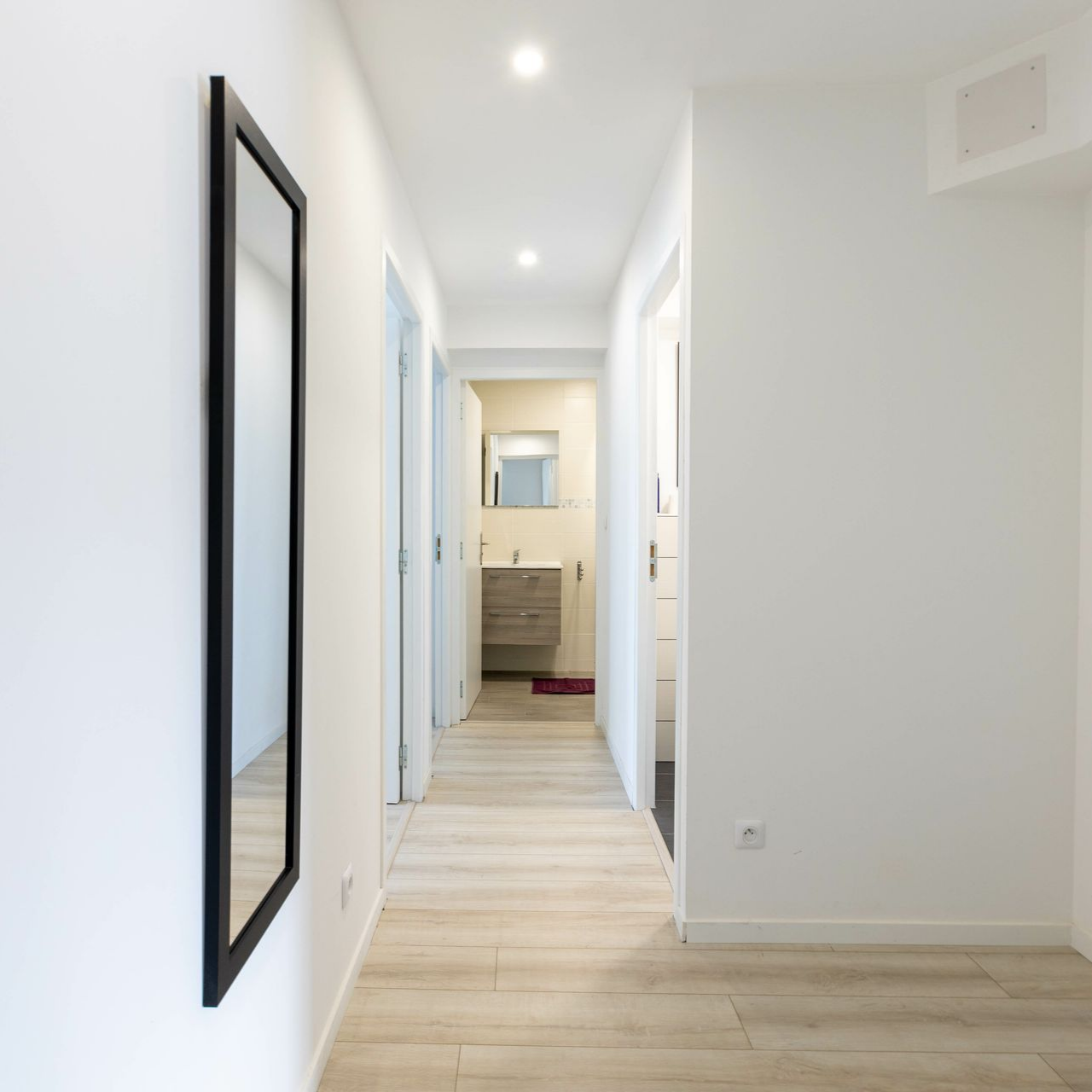 Couloir d'une maison avec les murs blancs et une salle de bains au fond.