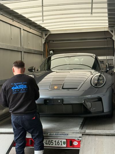 Ein Abschleppwagen verlädt an einem sonnigen Tag einen weissen Pkw auf einem Parkplatz mit mehreren anderen Fahrzeugen.
