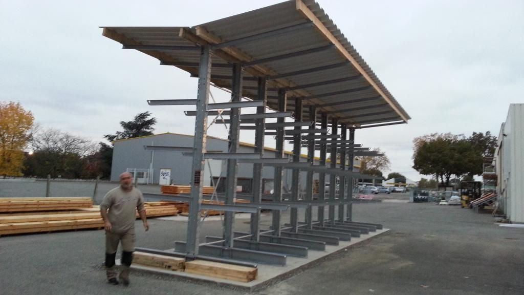 Un homme se tient près d'un grand râtelier à bois métallique à toit incliné dans une zone industrielle.