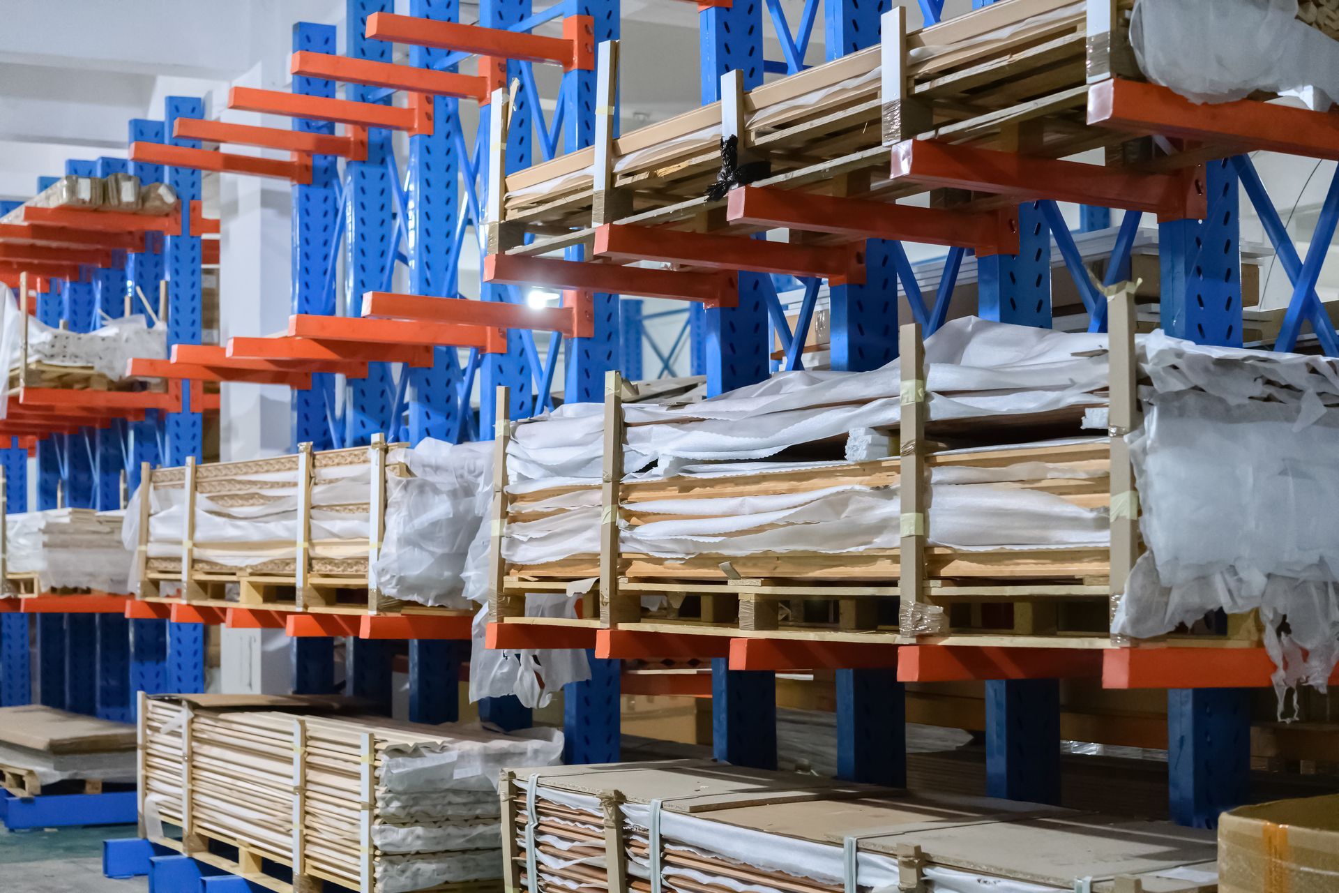 Rayonnages industriels cantilever bleus et orange chargés de caisses en bois et de matériaux emballés.