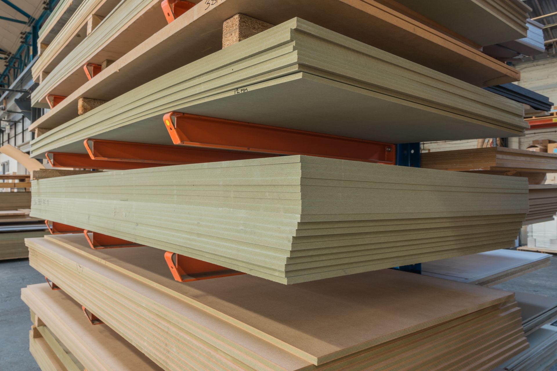 Des piles de planches de bois beige sur des étagères orange et bleues dans un entrepôt.