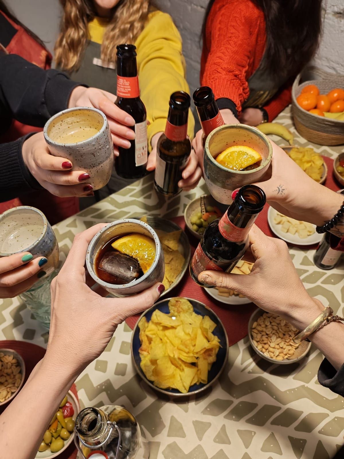 Un grupo de personas brinda con botellas y vasos alrededor de una mesa llena de cuencos con aperitivos.