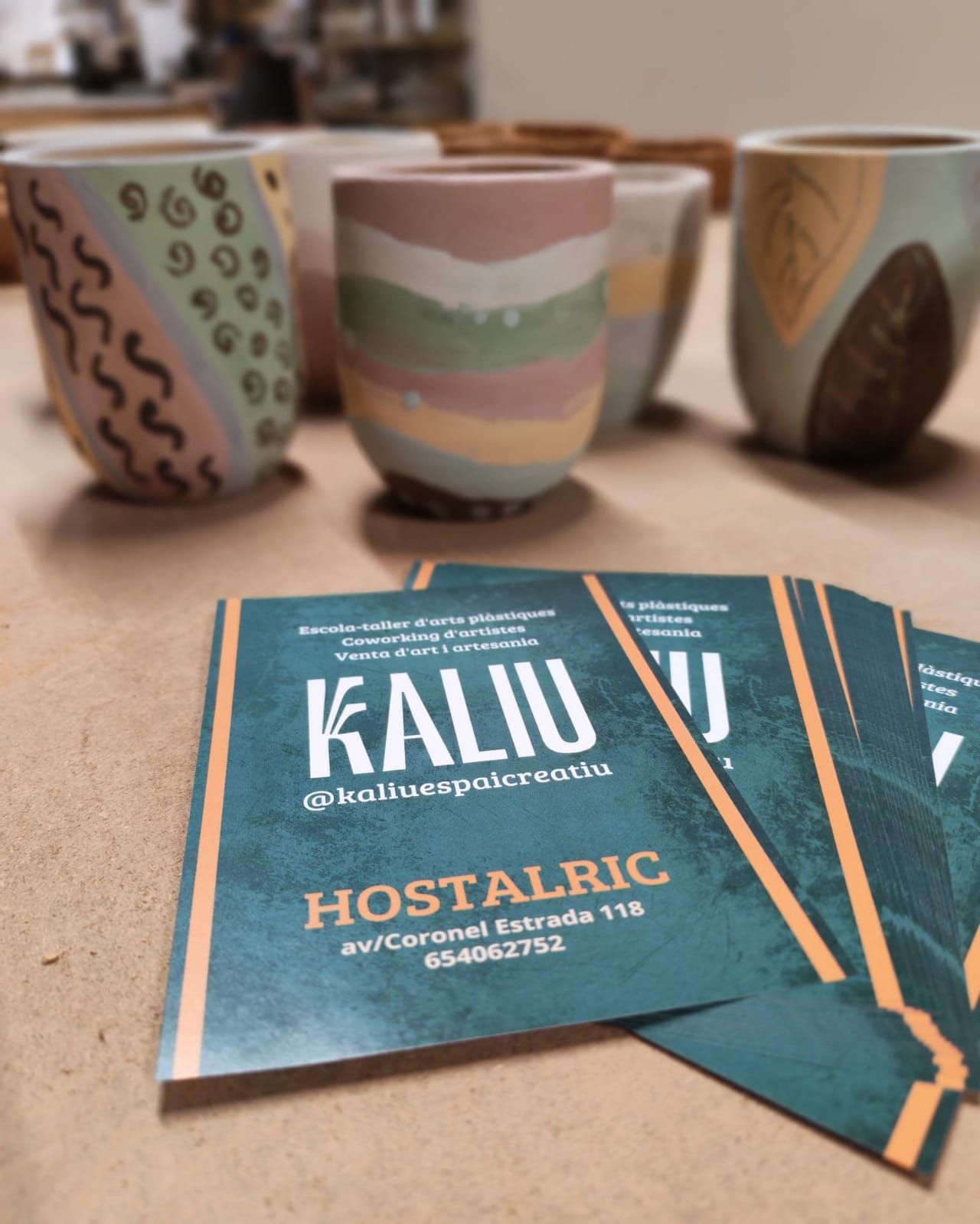 Tazas de cerámica hechas a mano con varios diseños, dispuestas detrás de tarjetas de visita de 