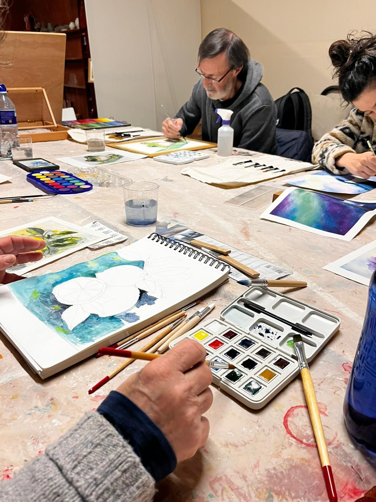 Personas en una mesa de taller pintando con acuarelas sobre papel.