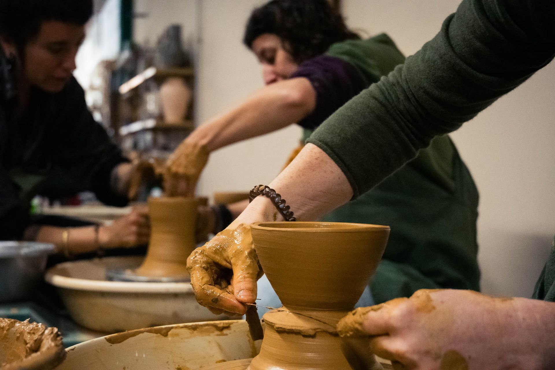 Dos personas dan forma a vasijas de arcilla en tornos de alfarero en un taller.