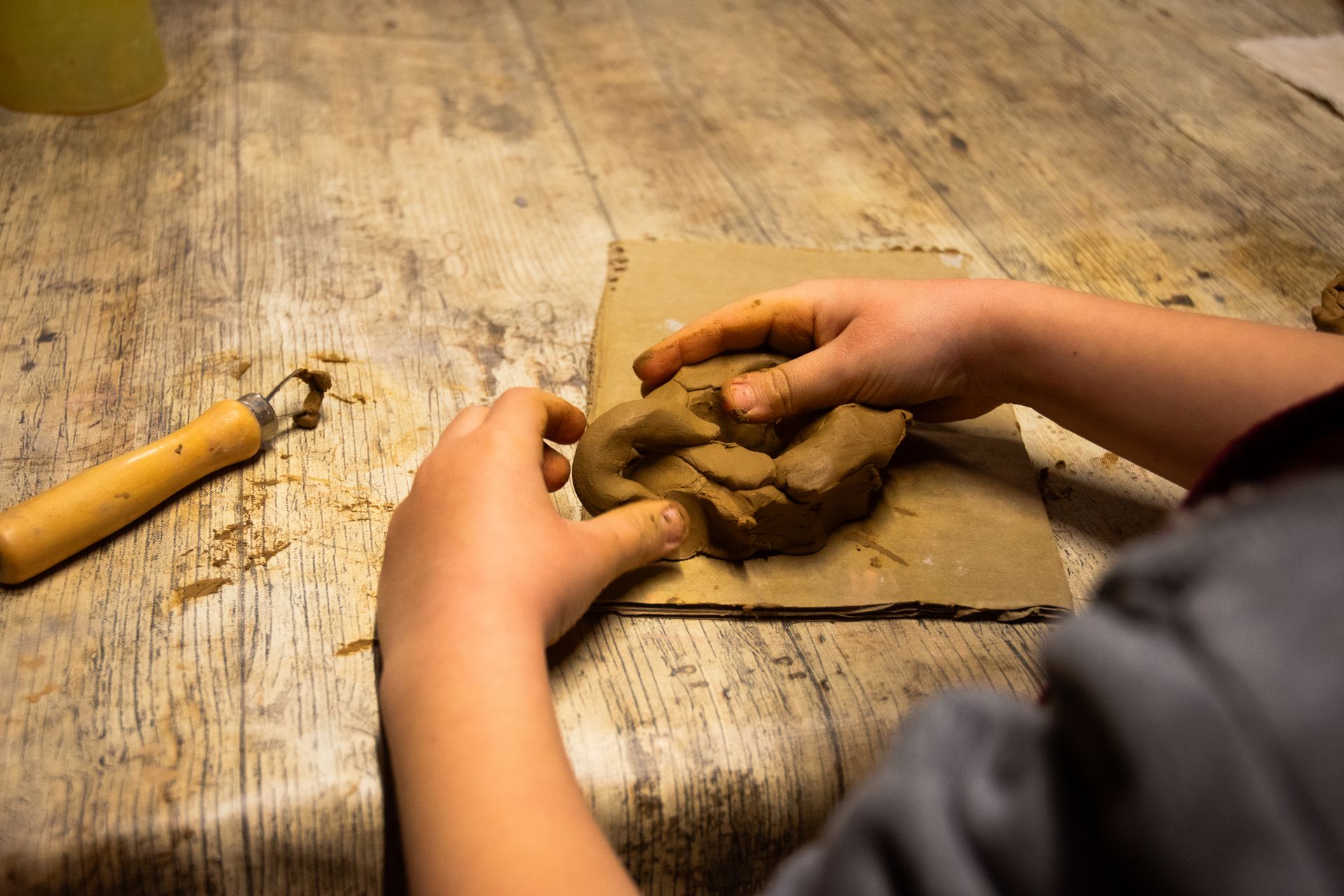 Petit test d'argila amb petites figures esculpides sobre una taula d'artesania, amb tasses i materials d'art borrosos al fons