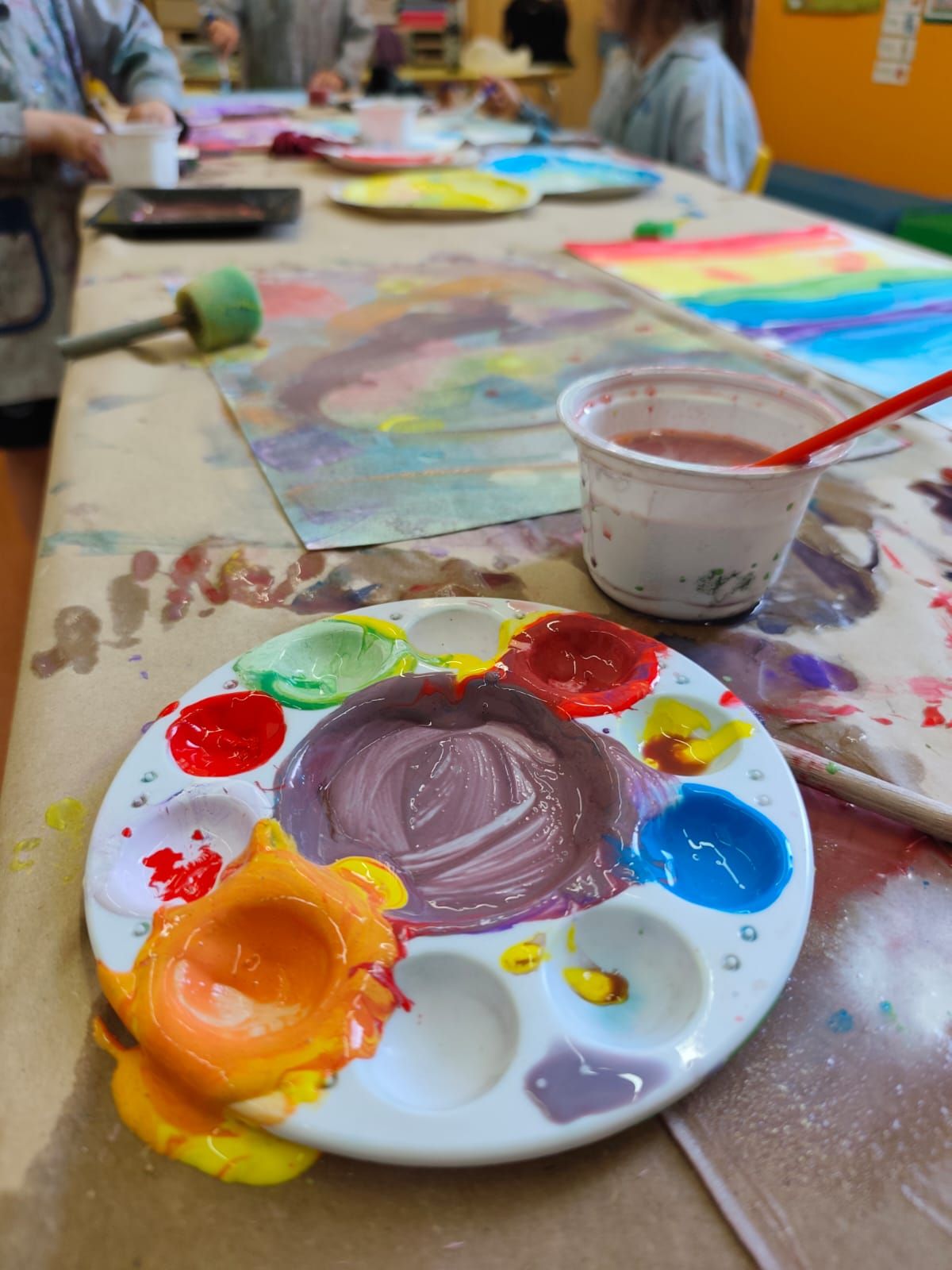 Nens pintant amb aquarel·les blaves a una taula, amb pinzells, paper i materials d'art de colors a prop